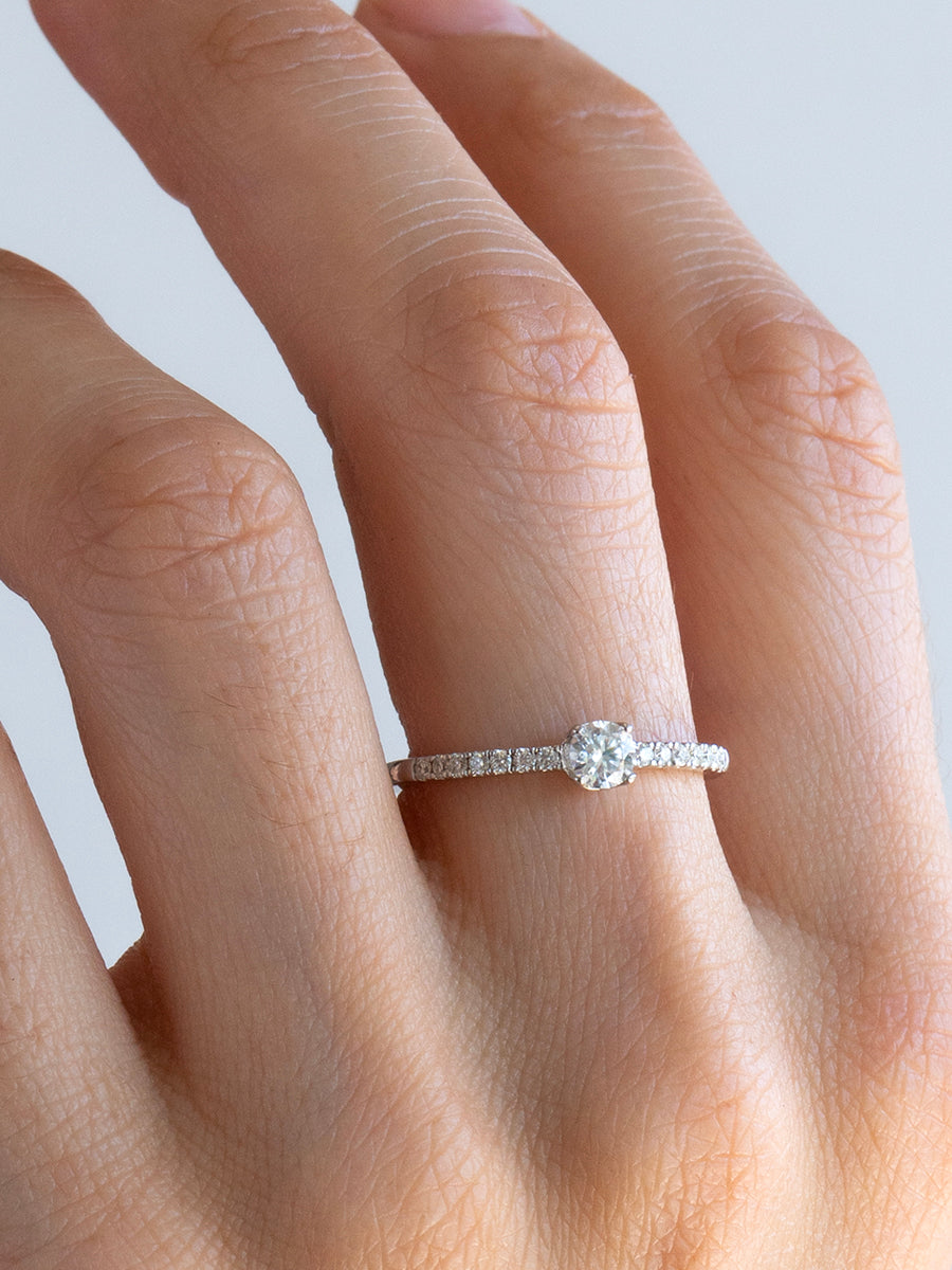 Anillo de compromiso delicado con moissanita central y laterales brillantes de plata rodinada.