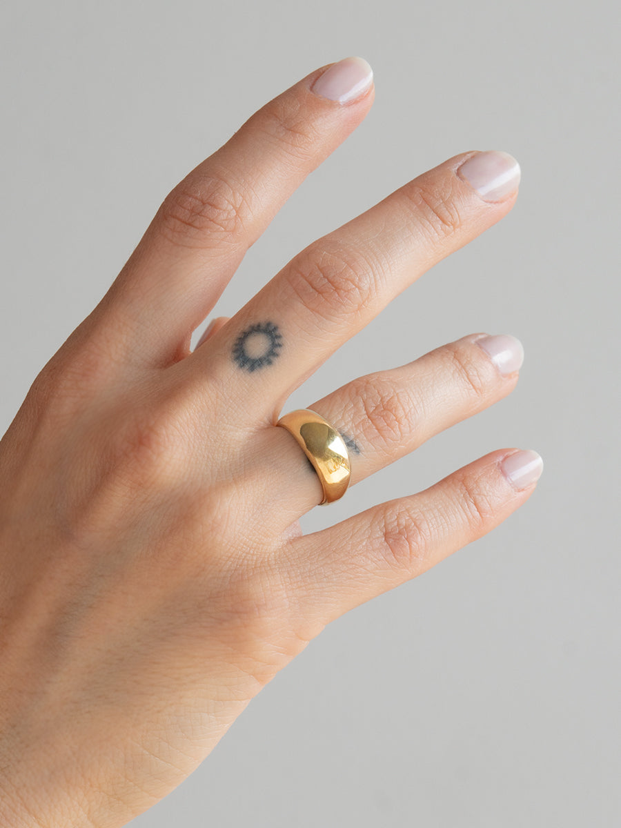 Anillo Alex de bronce macizo dorado de estilo grueso y minimalista (anillo ancho hecho a mano) luciendo en el dedo medio sobre fondo gris.