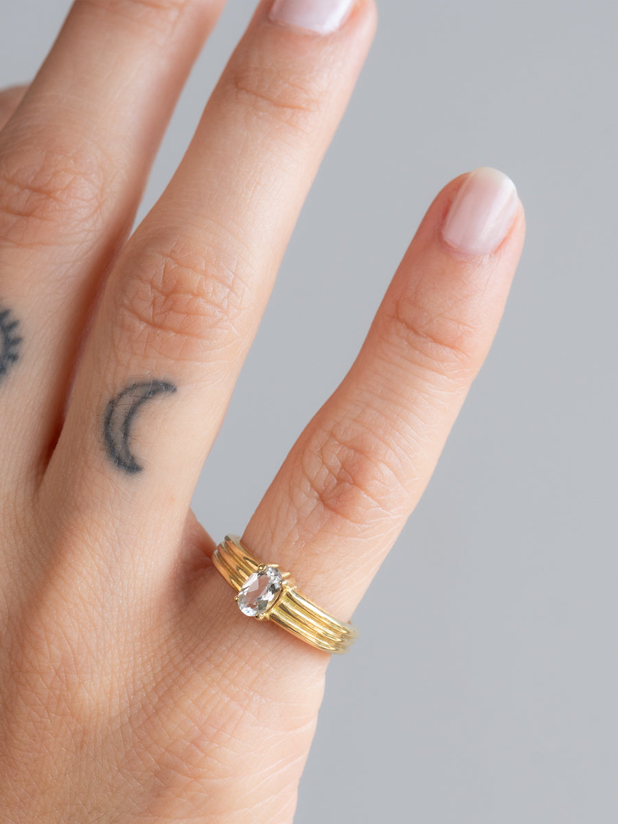 Anillo Inti de bronce macizo hecho a mano con un topacio blanco natural de corte oval sobre una banda con relieve, lucido en la mano de una modelo.