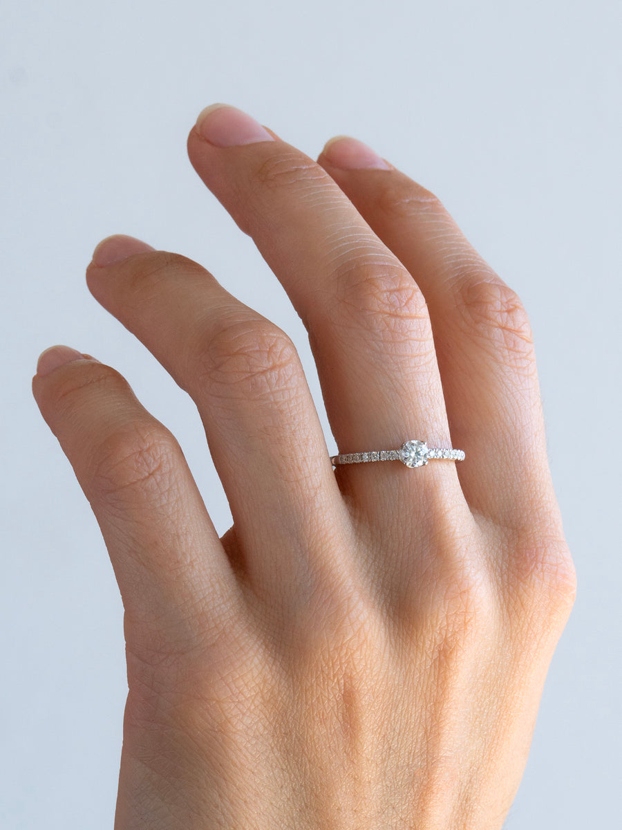 Anillo de compromiso delicado con moissanita central y laterales brillantes de plata rodinada.